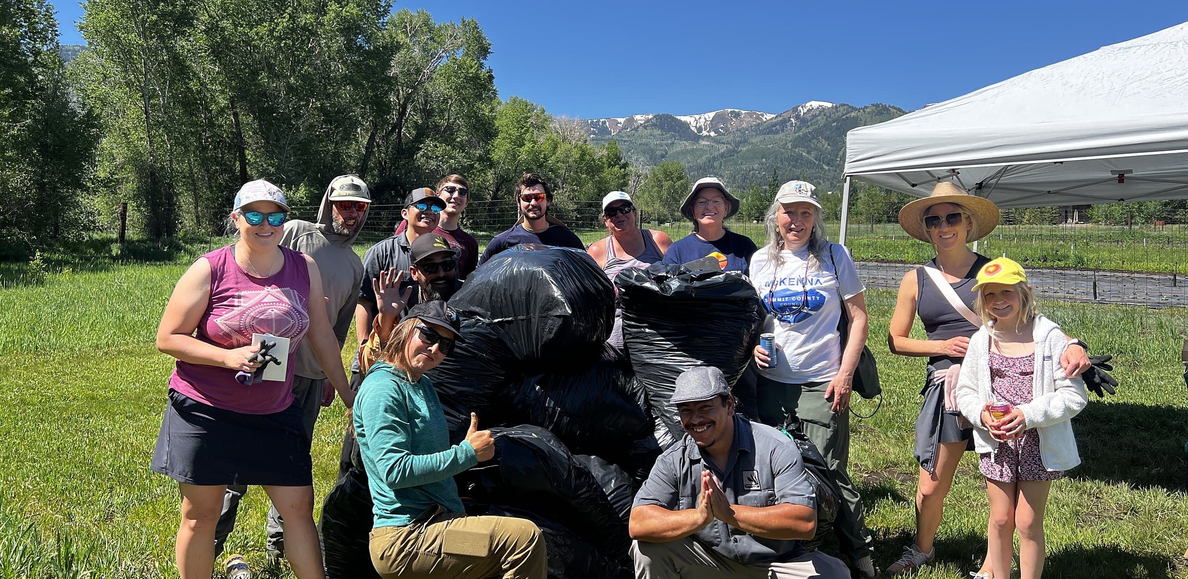 Garlic Mustard Games volunteers gathered behind their bagged haul, mountains in the distance